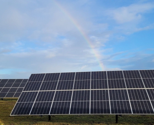 A rainbow over a field with solar panels.